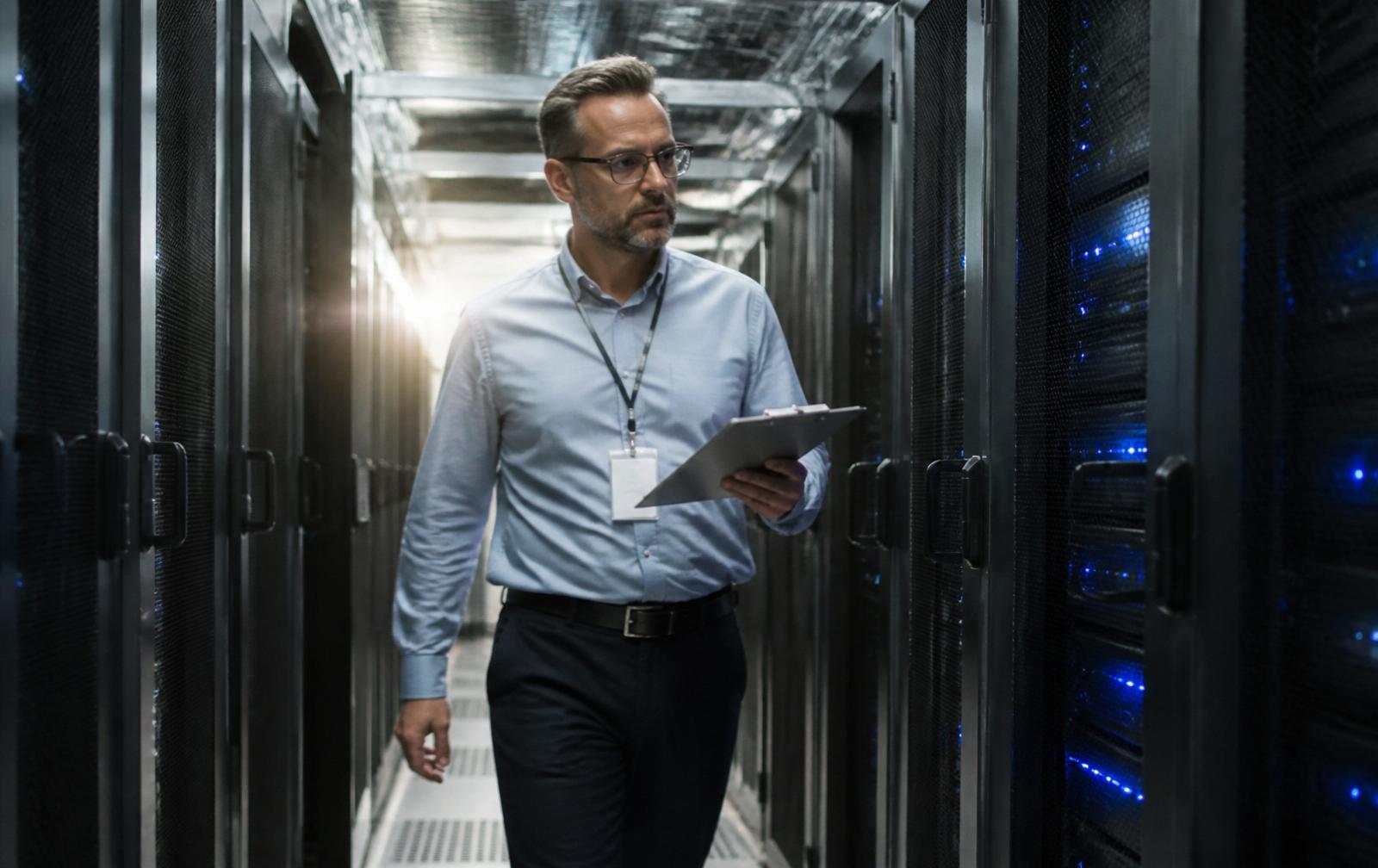 Facility manager with a clipboard walking a data center aisle inspecting server racks.