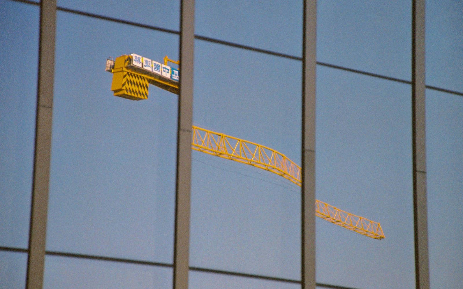 Construction crane reflected in the facade of a nearly completed commercial building.